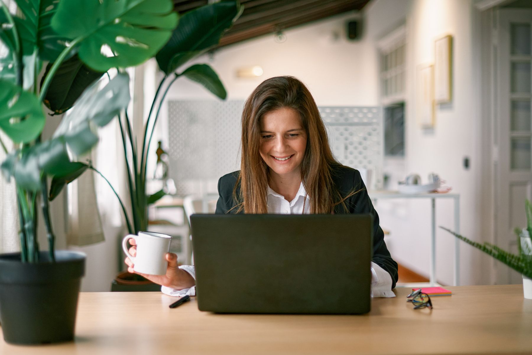 Blije zakenvrouw met laptop, planten en koffie